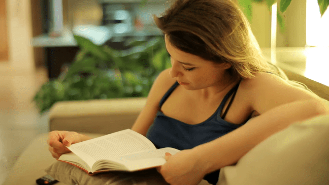 woman-reading-a-book-and-sitting-on-a-sofa-at-night-in-room_4yn6d7l9__F0000